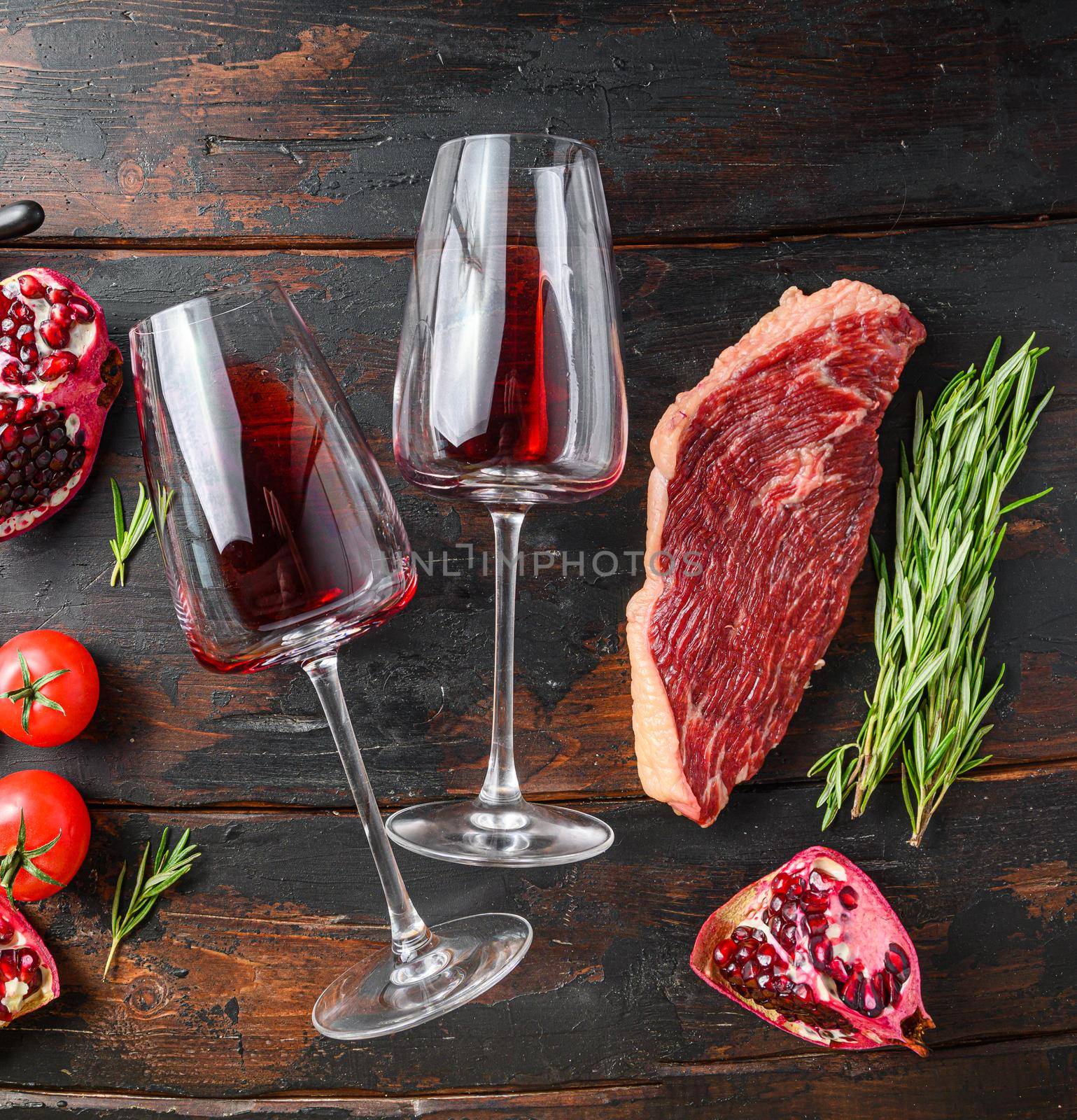 Two glass of red wine near raw beef steak over old dark wooden table top view. Big size