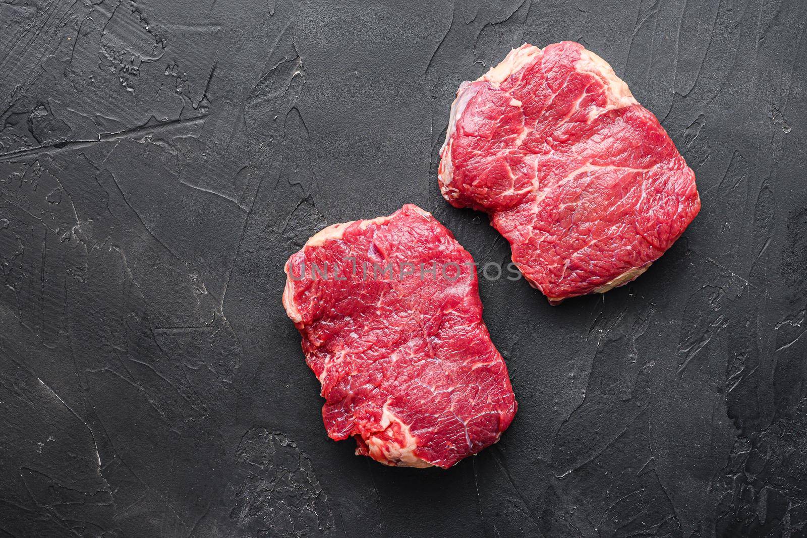 Organic rump steaks over black background, top view with space for text