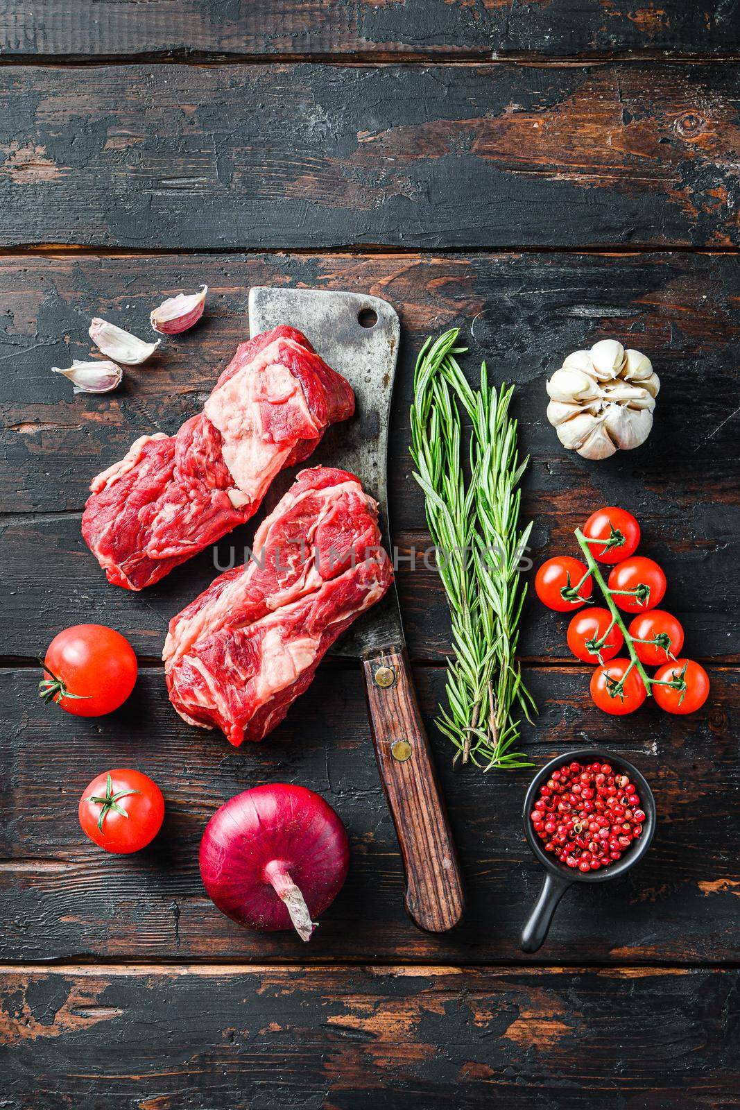 Organic raw chuck eye roll beef steak cut with rosemary red onin, garlic peppercorns and tomatoes on old dark wooden table. Top view