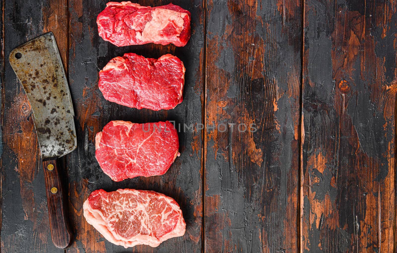 A set of different types of raw beef steaks:top blade, rump, chuck eye roll over old wooden background top view with butcher cleaver space for text