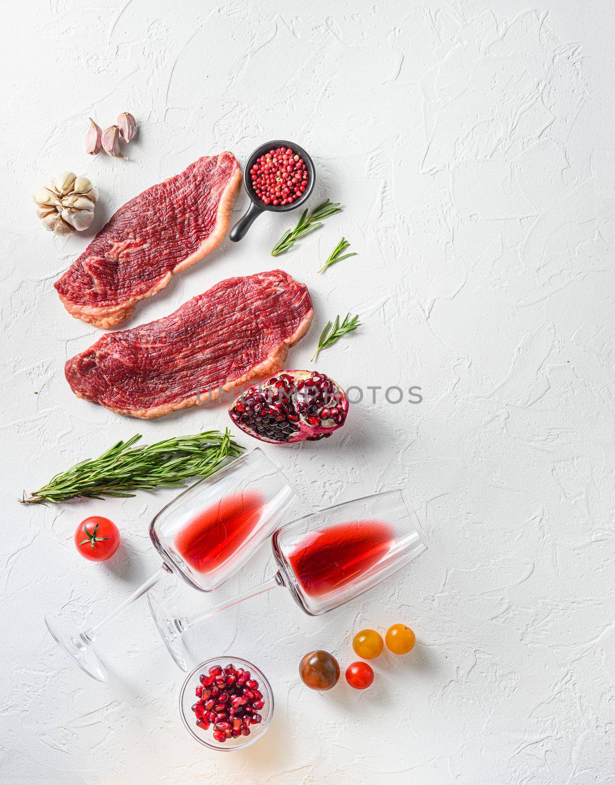 Raw picanha steak with glasses of red wine , herbs and pomegranate top view over white textured background . Big size