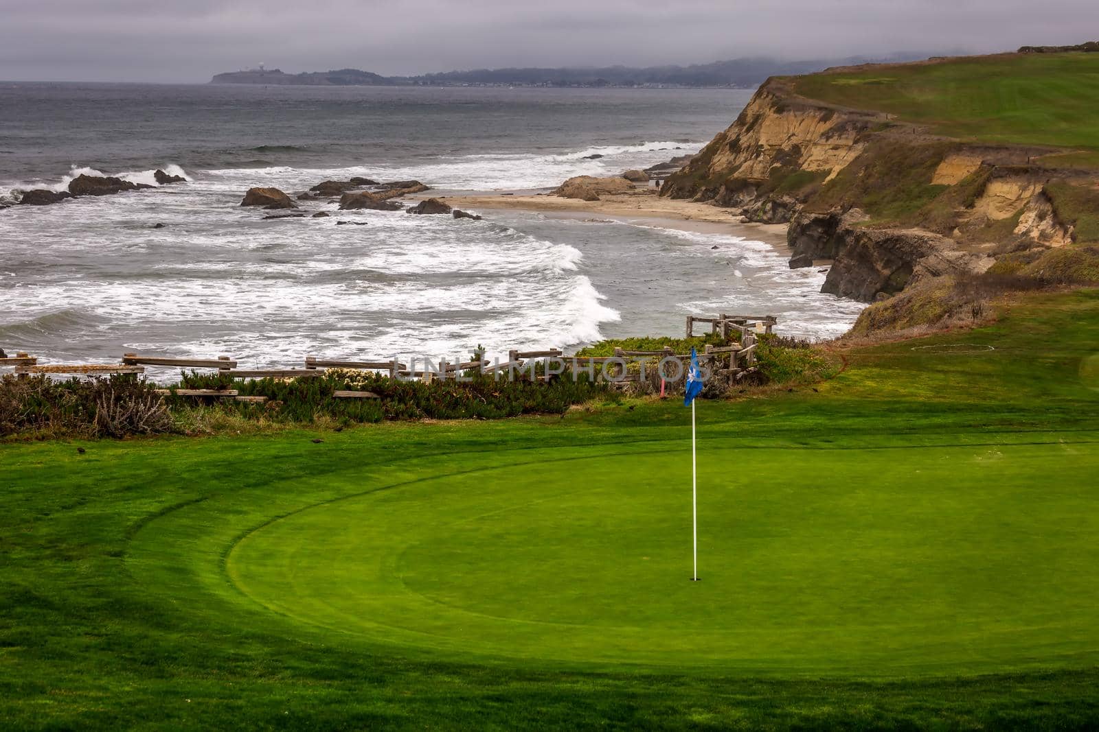 Golf course putting green and cliffs by the pacific ocean bay. Half Moon Bay California. Villas and houses.