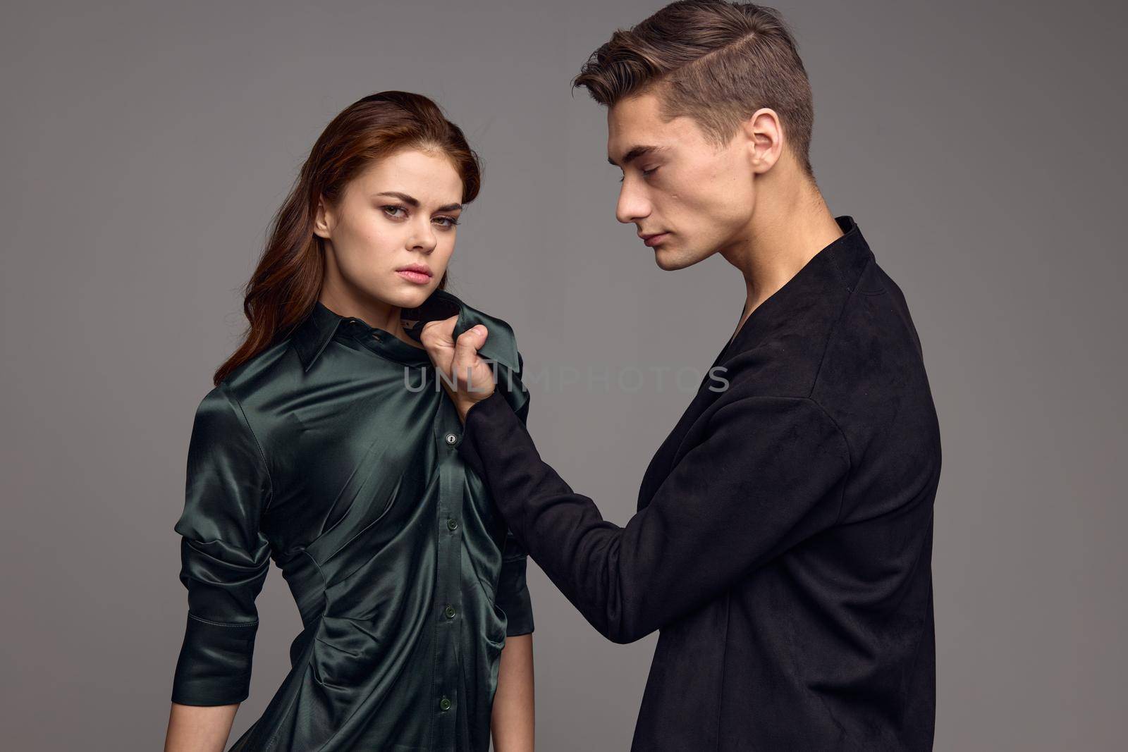 An angry man holds a woman by the collar of a dress on a gray background domestic violence. High quality photo