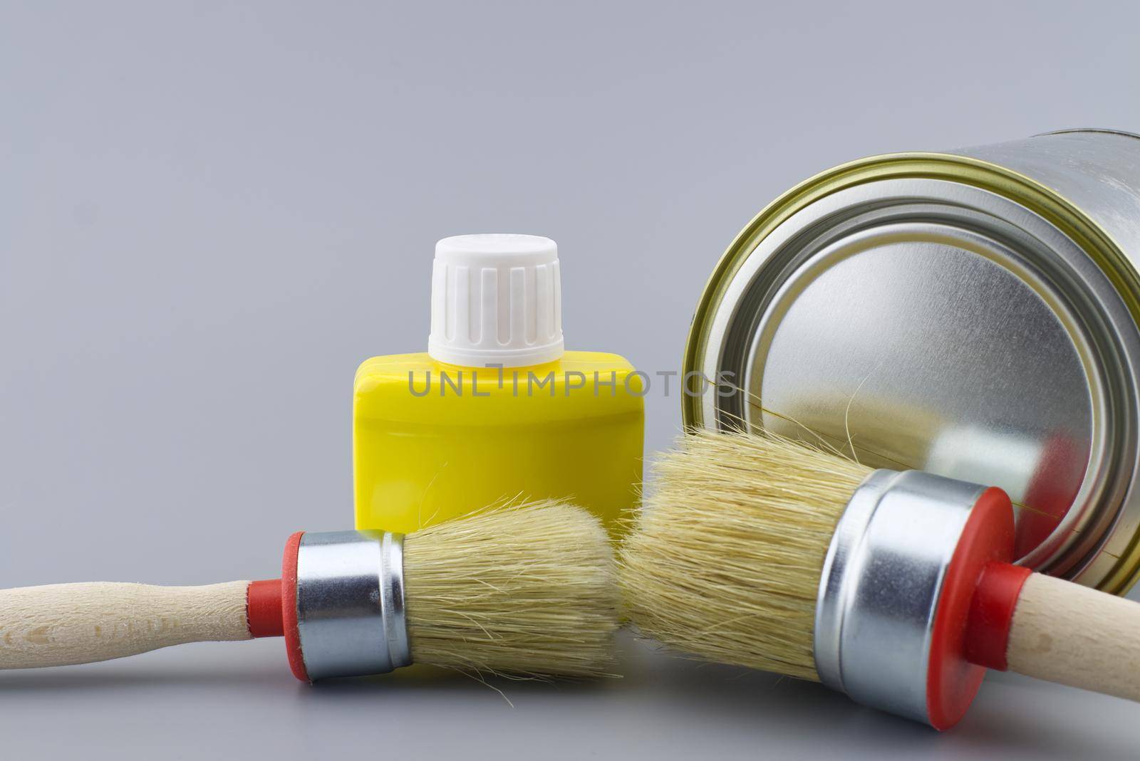 New color, decorating or renovations concept with a still life with assorted clean paint brushes and unlabeled tin of paint over a grey background