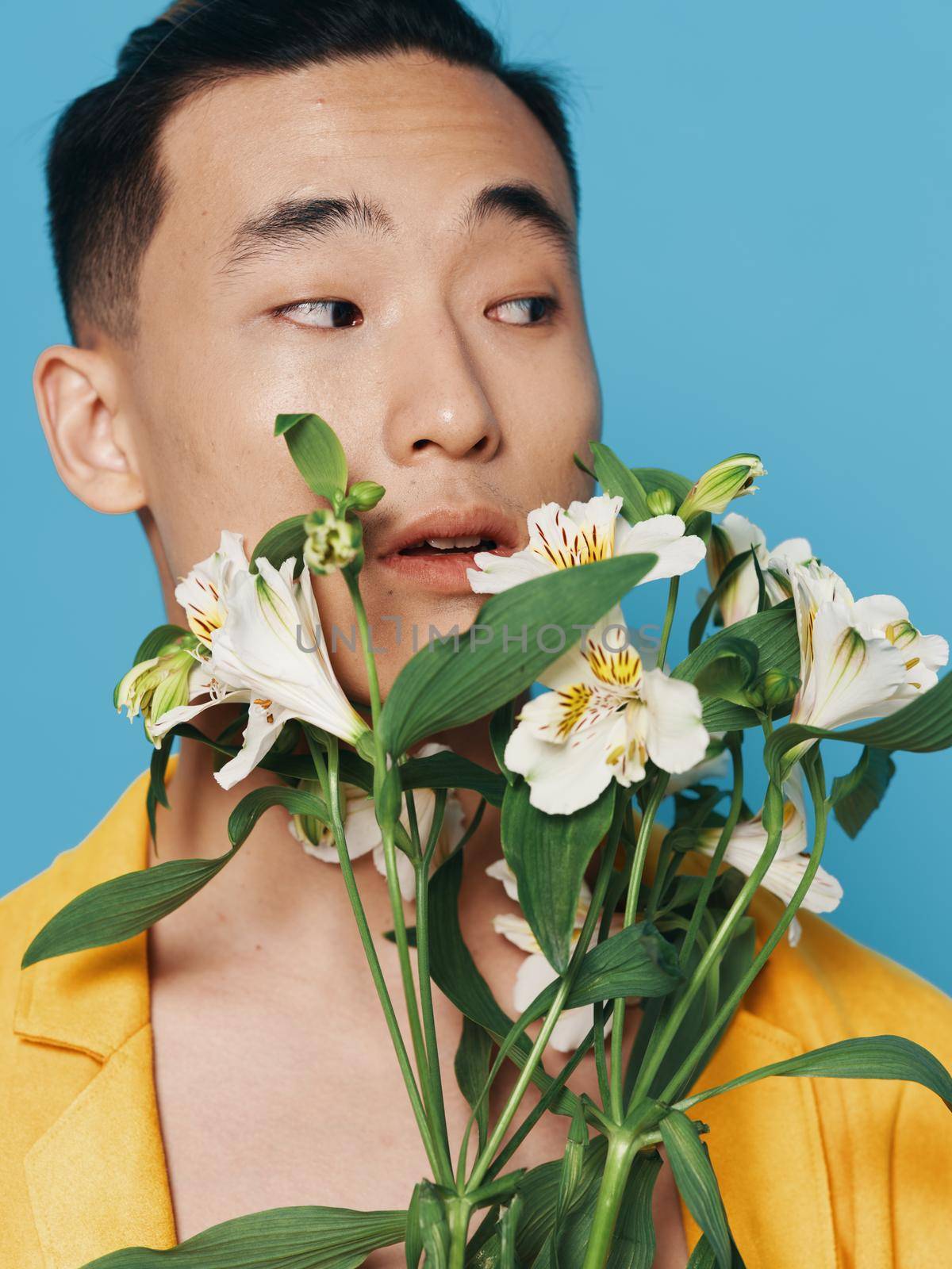 romantic asian guy with a bouquet of white flowers and in a yellow coat model. High quality photo