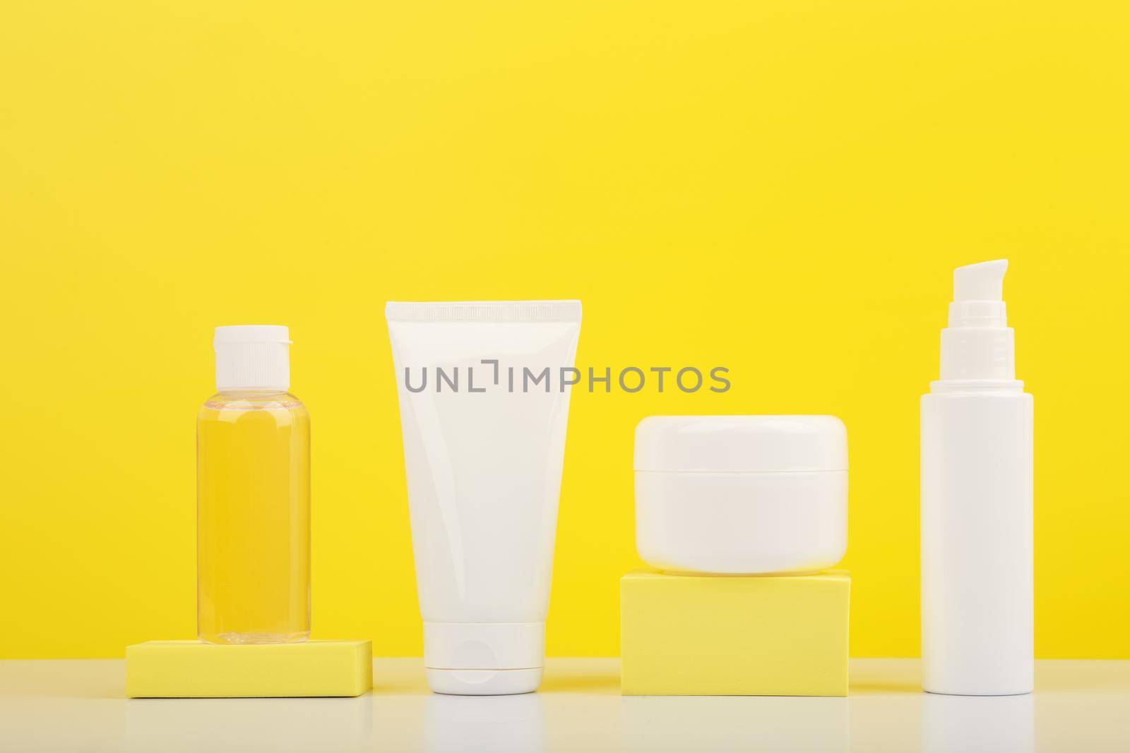 Still life with set of cosmetic containers on white glossy table against bright yellow background. . Concept of everyday skin care for smooth, young looking skin