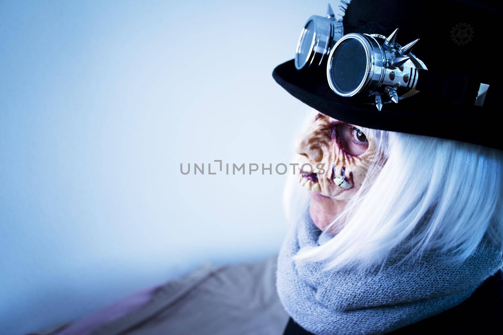 Woman with monster face and black hat wearing steampunk glasses. White hair.