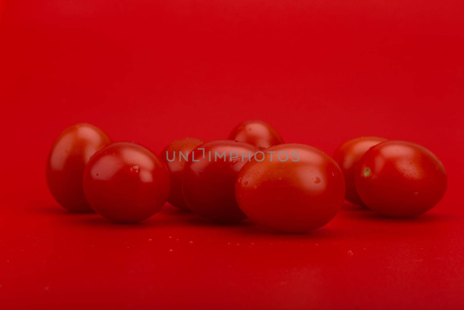Bunch of tomatoes with water drops against red background with copy space by Senorina_Irina