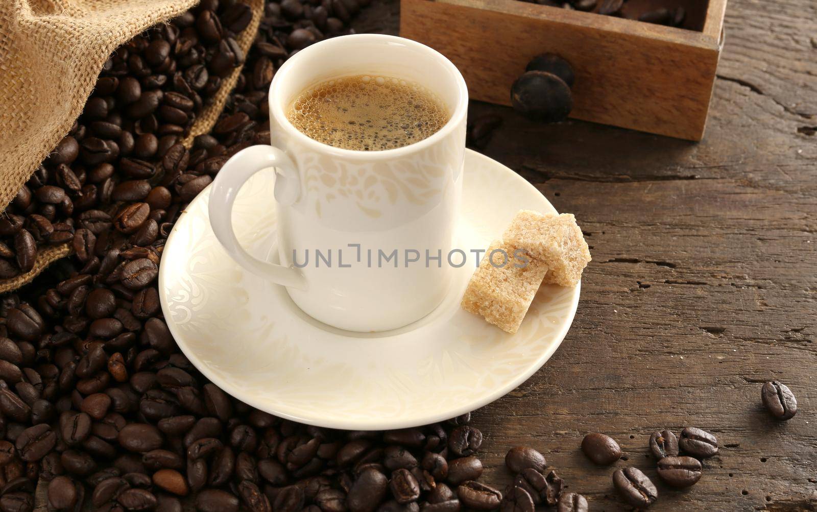 Rustic background with cup of coffee espresso in white porcelain cup with roasted coffee beans on old wooden background with canvas bag