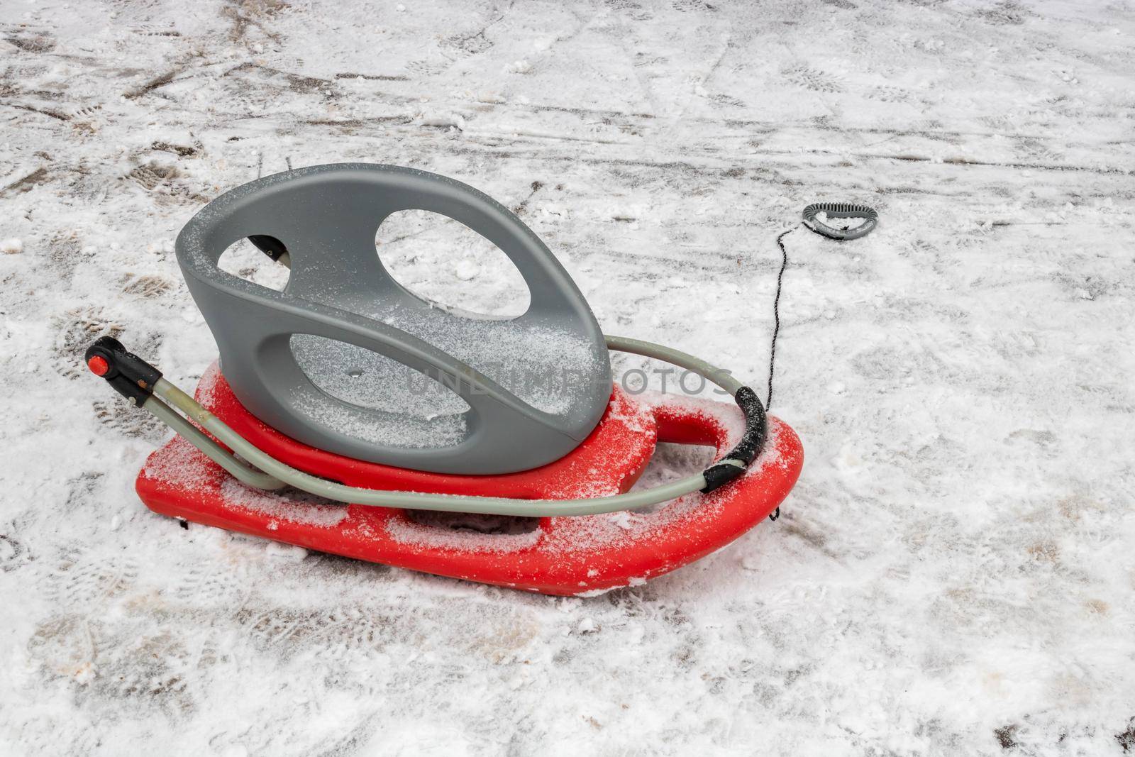 Red-gray plastic snow sled on the snow on the road by lapushka62