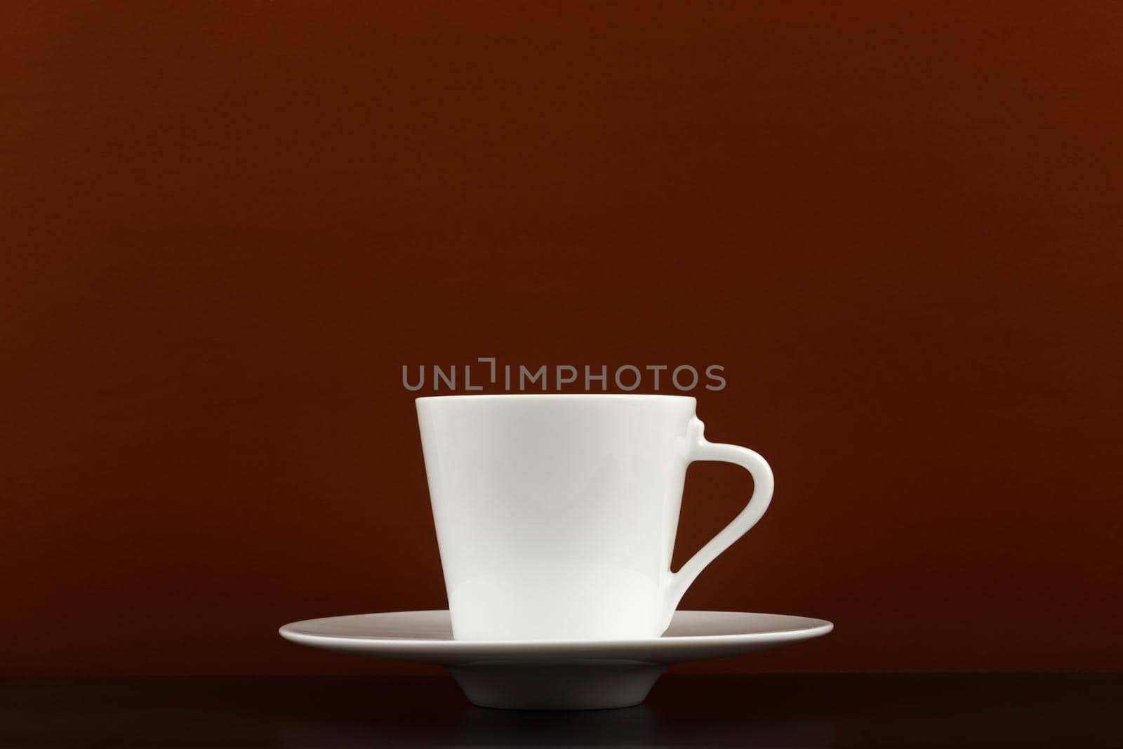 Minimalistic dark still life with white glossy cup of coffee on black table against dark brown background with copy space. High quality photo