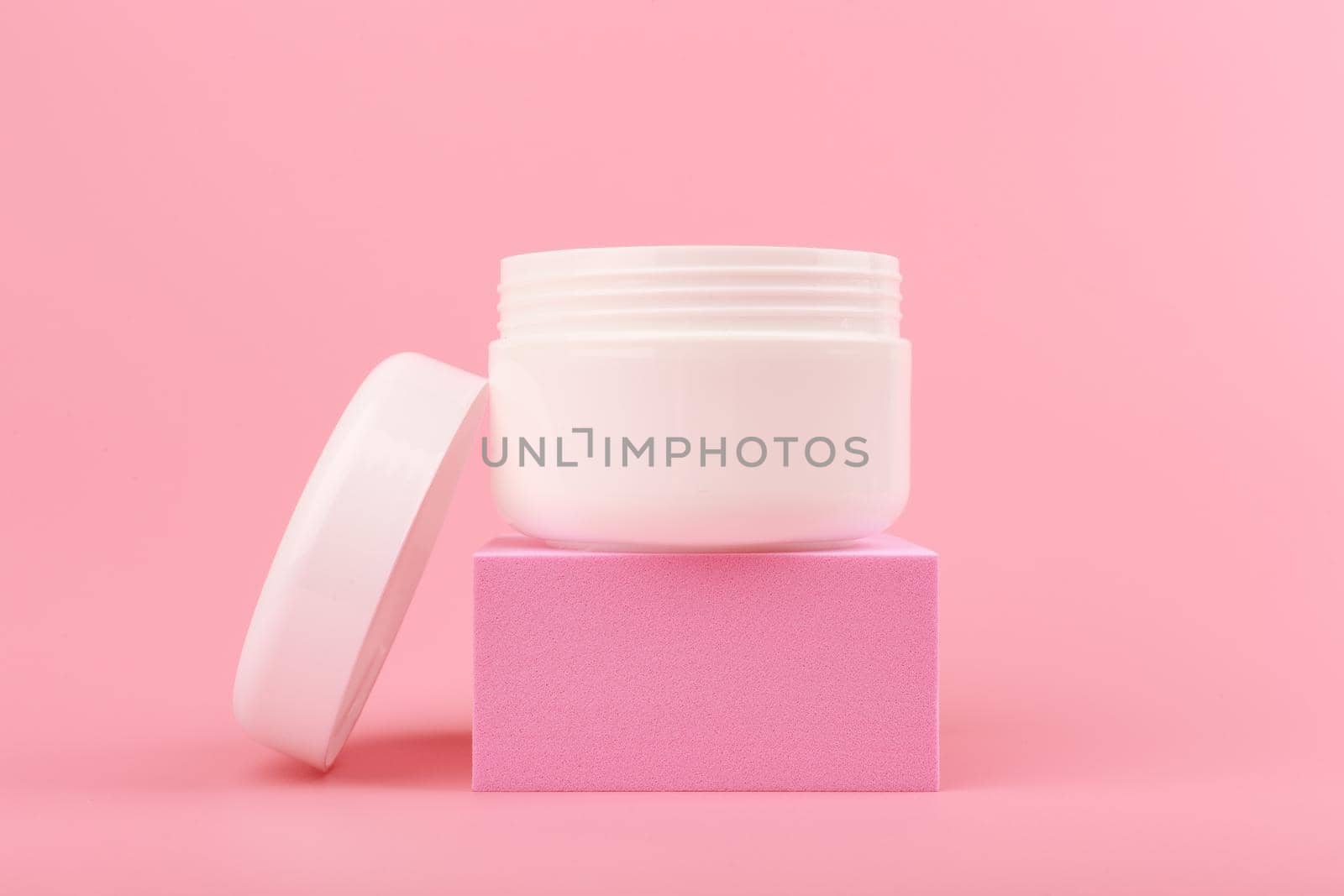 Close up of face cream. mask or balm in white jar with opened cap on pink podium against pink background by Senorina_Irina