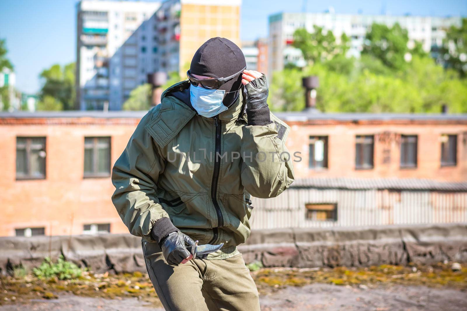 A masked criminal with a knife in his hands is trying to hide from pursuit