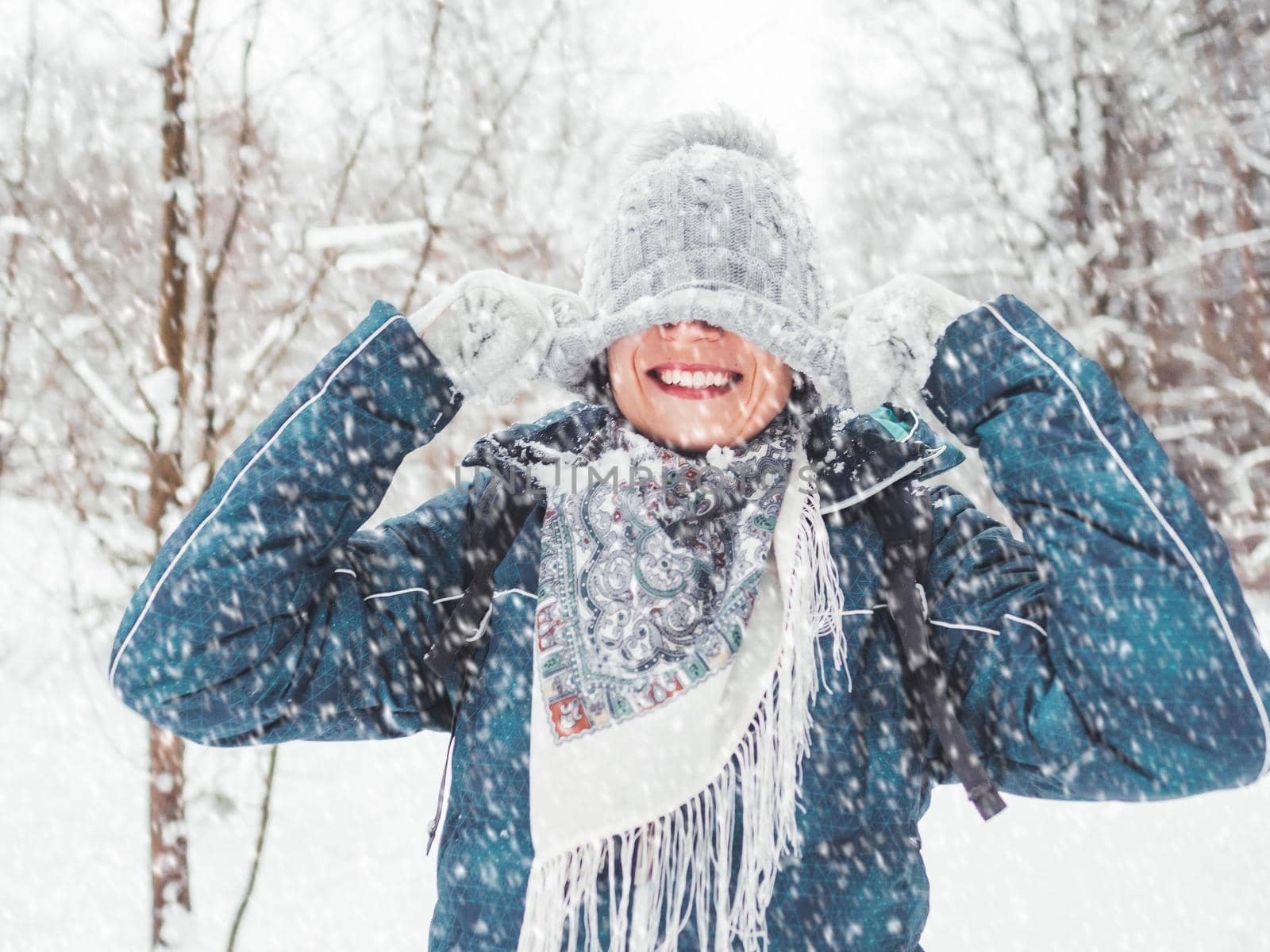 Smiling woman is playing with knitted hat. Fun in snowy winter forest. Woman laughs as she walks through wood. Sincere emotions. by aksenovko