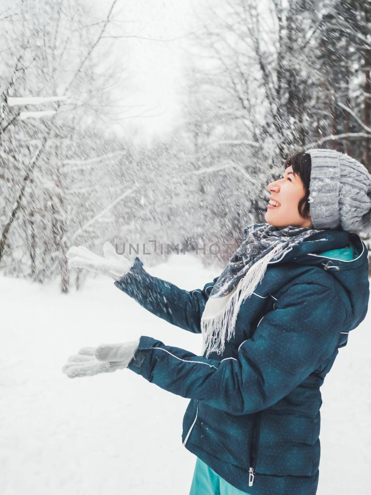Smiling woman is playing with snow. Fun in snowy winter forest. Woman laughs as she walks through wood. Sincere emotions.