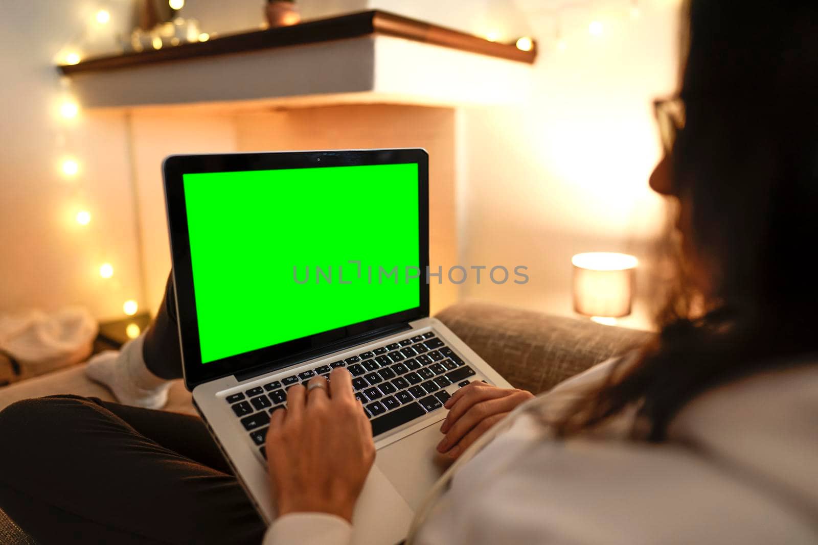 Working from home to change your life: side view close up of young female internet freelance using laptop with blank green screen display comfortably writing at notebook on her sofa. Focus on keyboard by robbyfontanesi