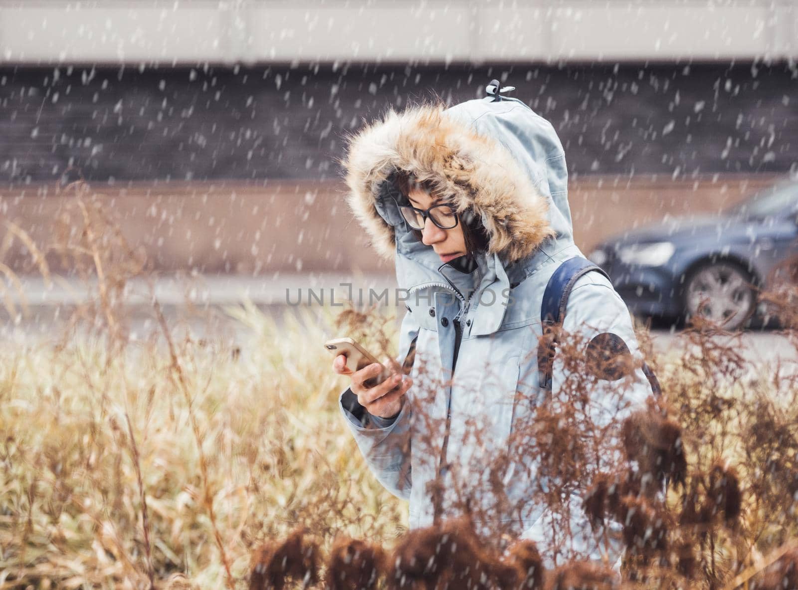 Smiling woman in light blue warm jacket is texting someone on smartphone. Online communication via LTE or Wi-fi. Wireless cellular technology. Autumn season in town. by aksenovko