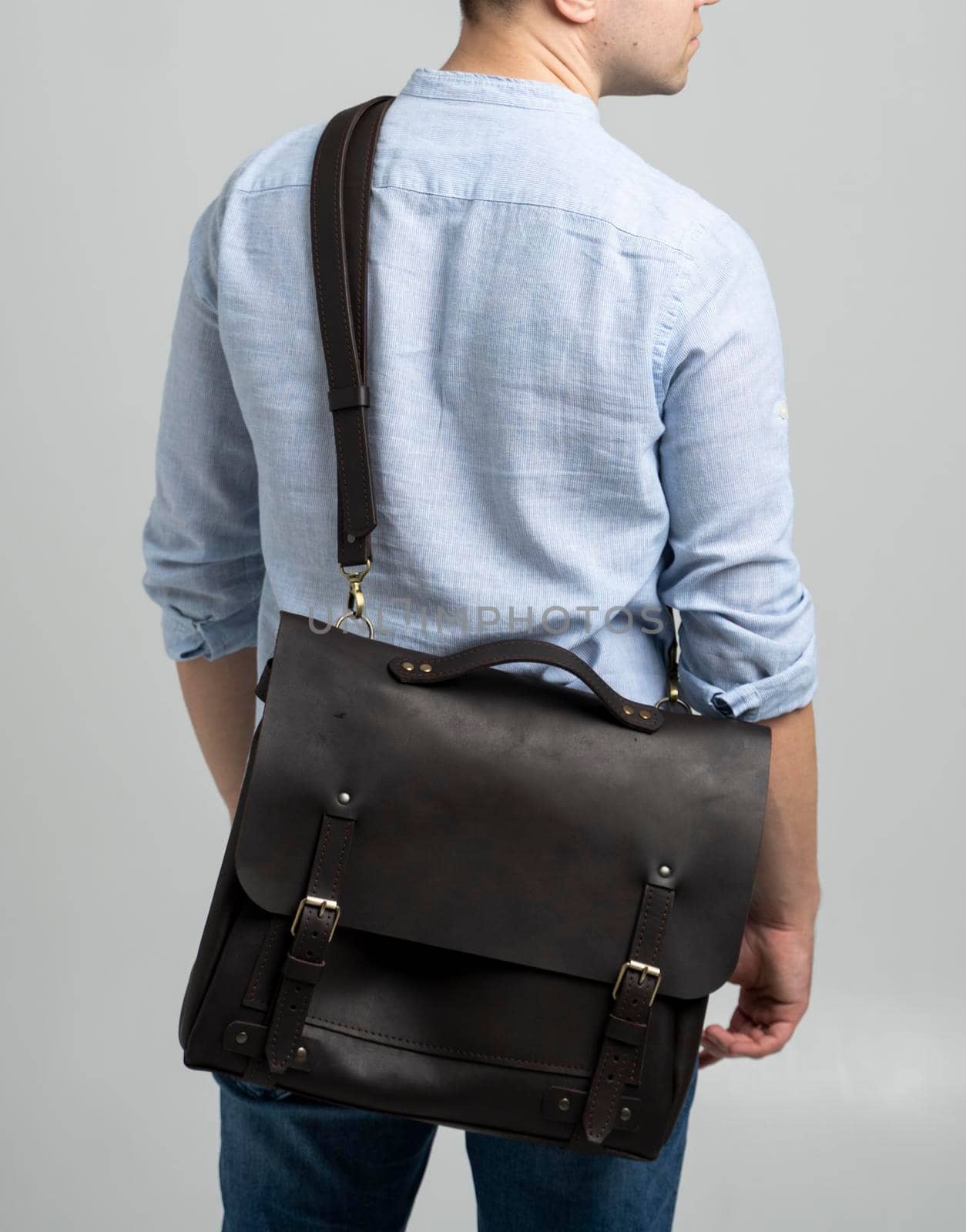 Brown men's shoulder leather bag for a documents and laptop on the shoulders of a man in a blue shirt and jeans with a white background. Satchel, mens leather handmade briefcase. by vovsht