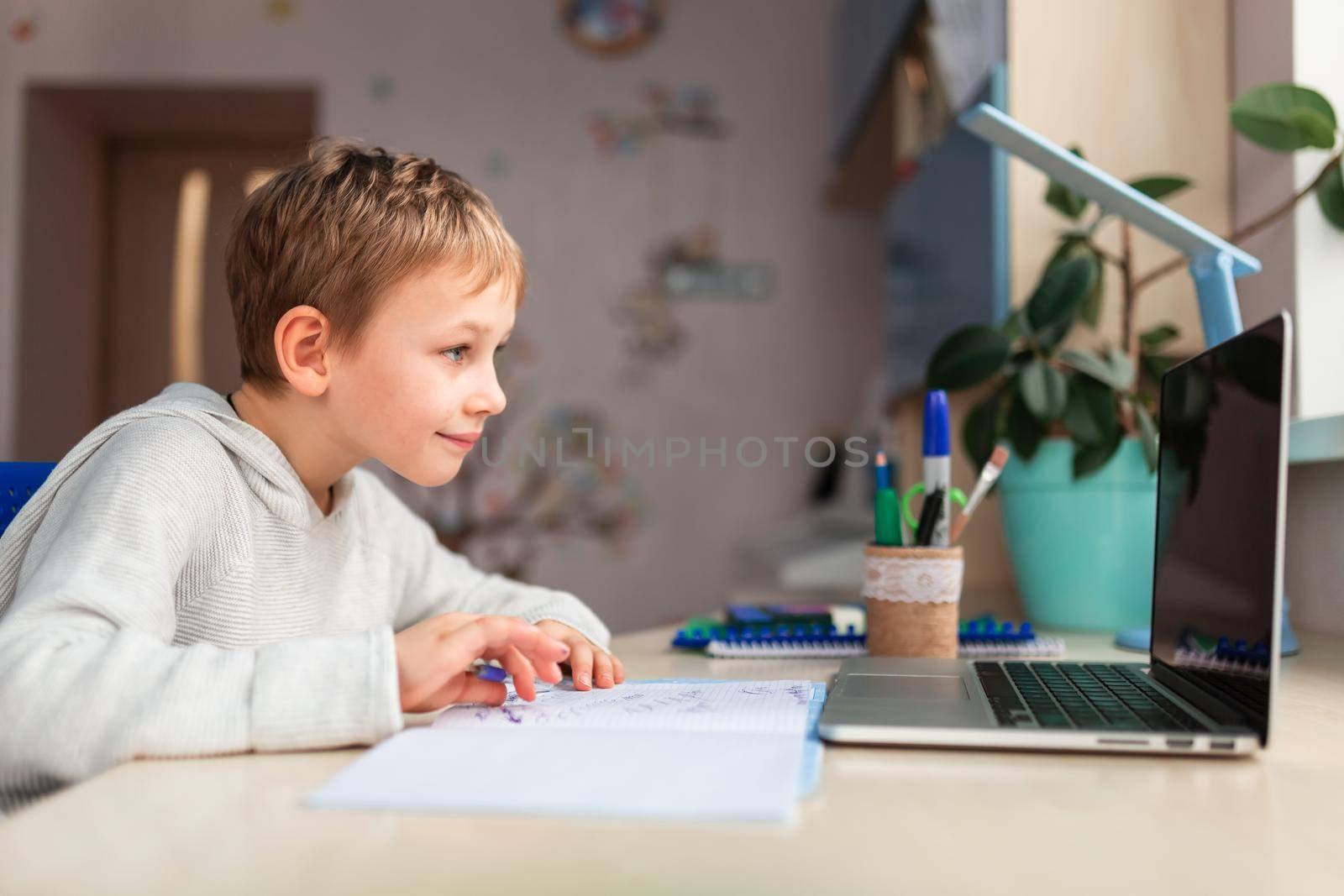 Cute little schoolboy studying at home doing school homework. Training books and notebook on the table. Distance learning online education