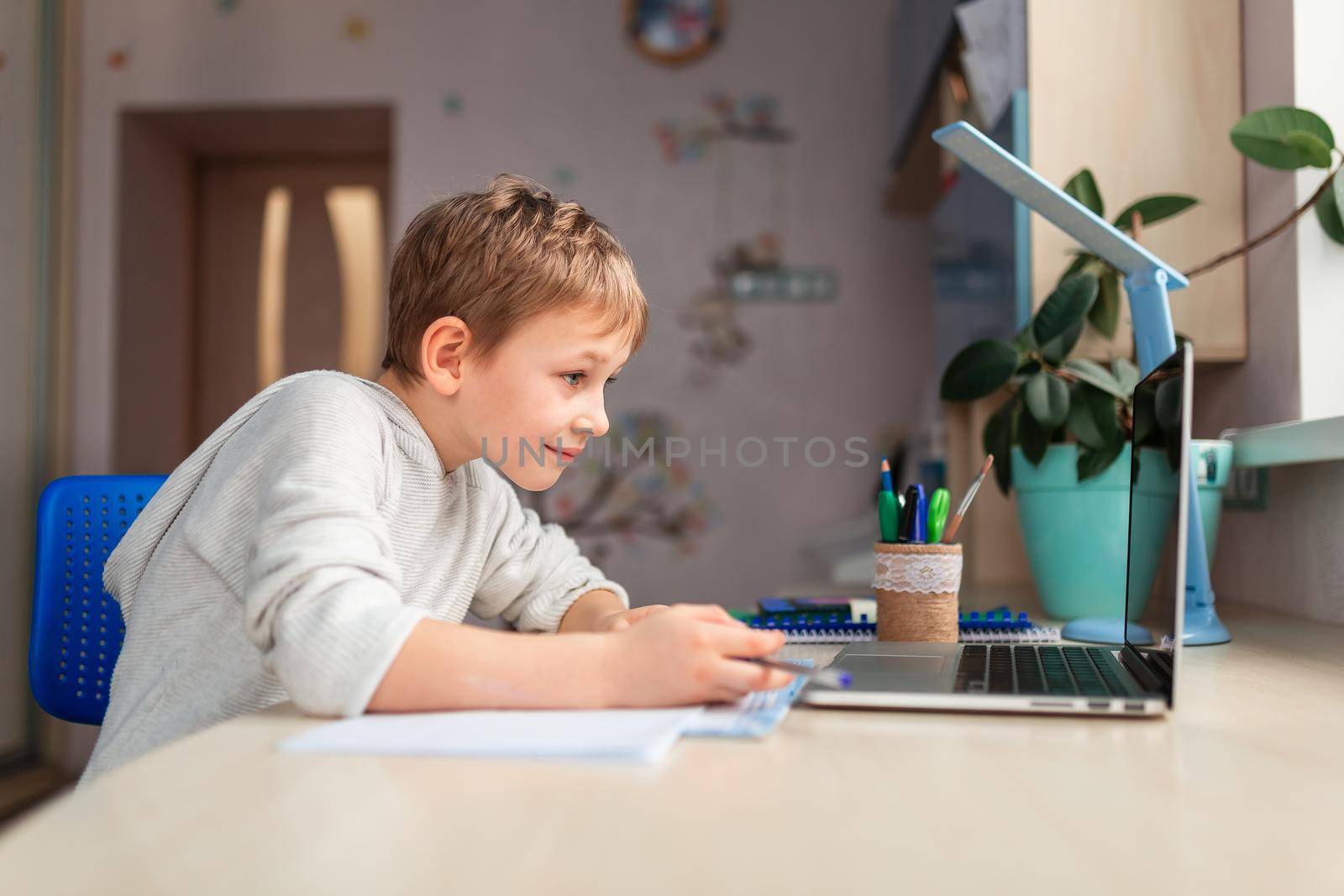 Cute little schoolboy studying at home doing school homework. Training books and notebook on the table. Distance learning online education