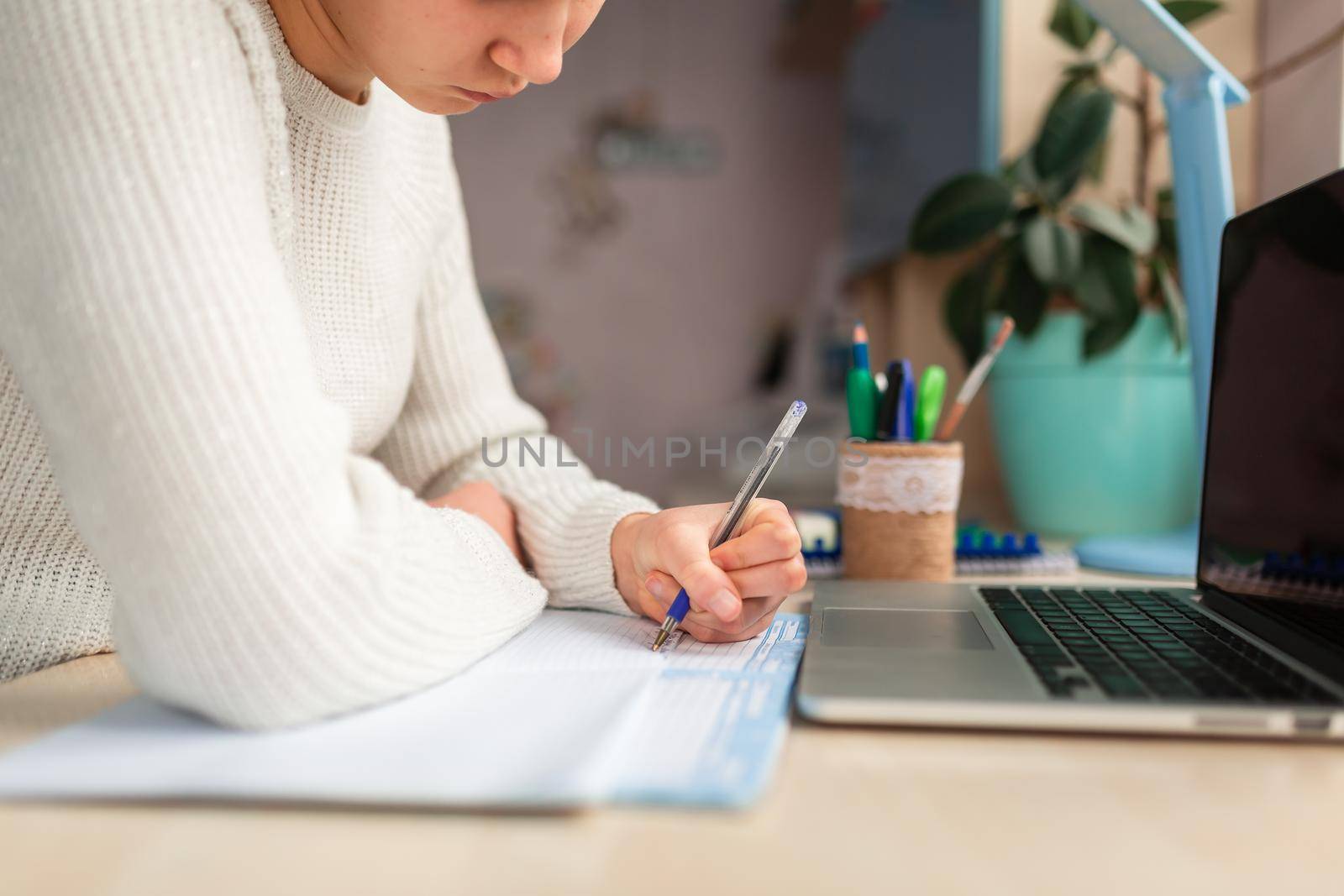 Beautiful schoolgirl studying at home doing school homework. Hand's close-up. Training books and notebook on the table. Distance learning online education