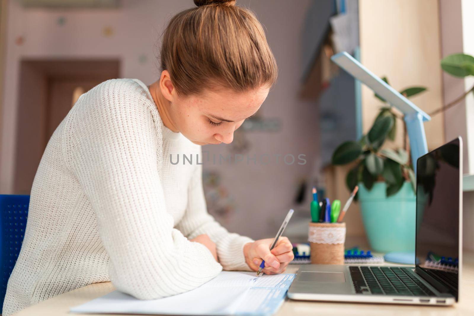 Beautiful schoolgirl studying at home doing school homework. Training books and notebook on the table. Distance learning online education