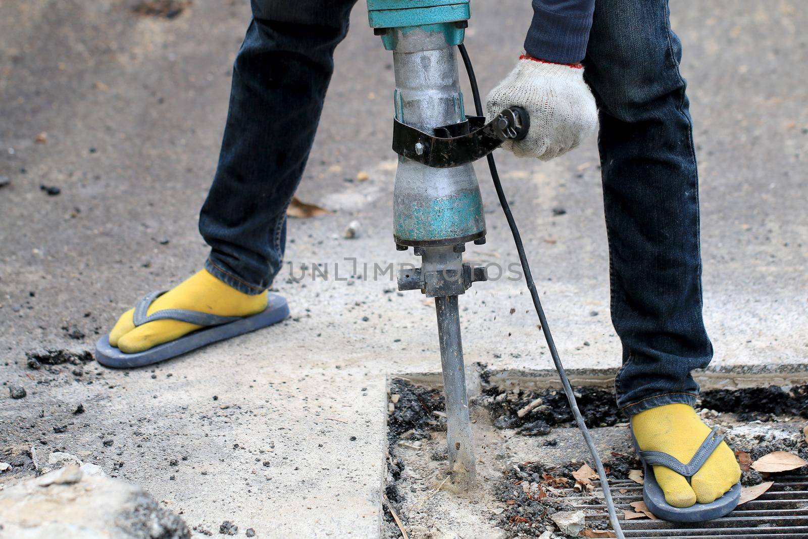 Male workers use electric concrete breaker for digging and drilling concrete repairing driveway surface with jackhammer at the local city road, during sidewalk, work construction site. by NarinNonthamand