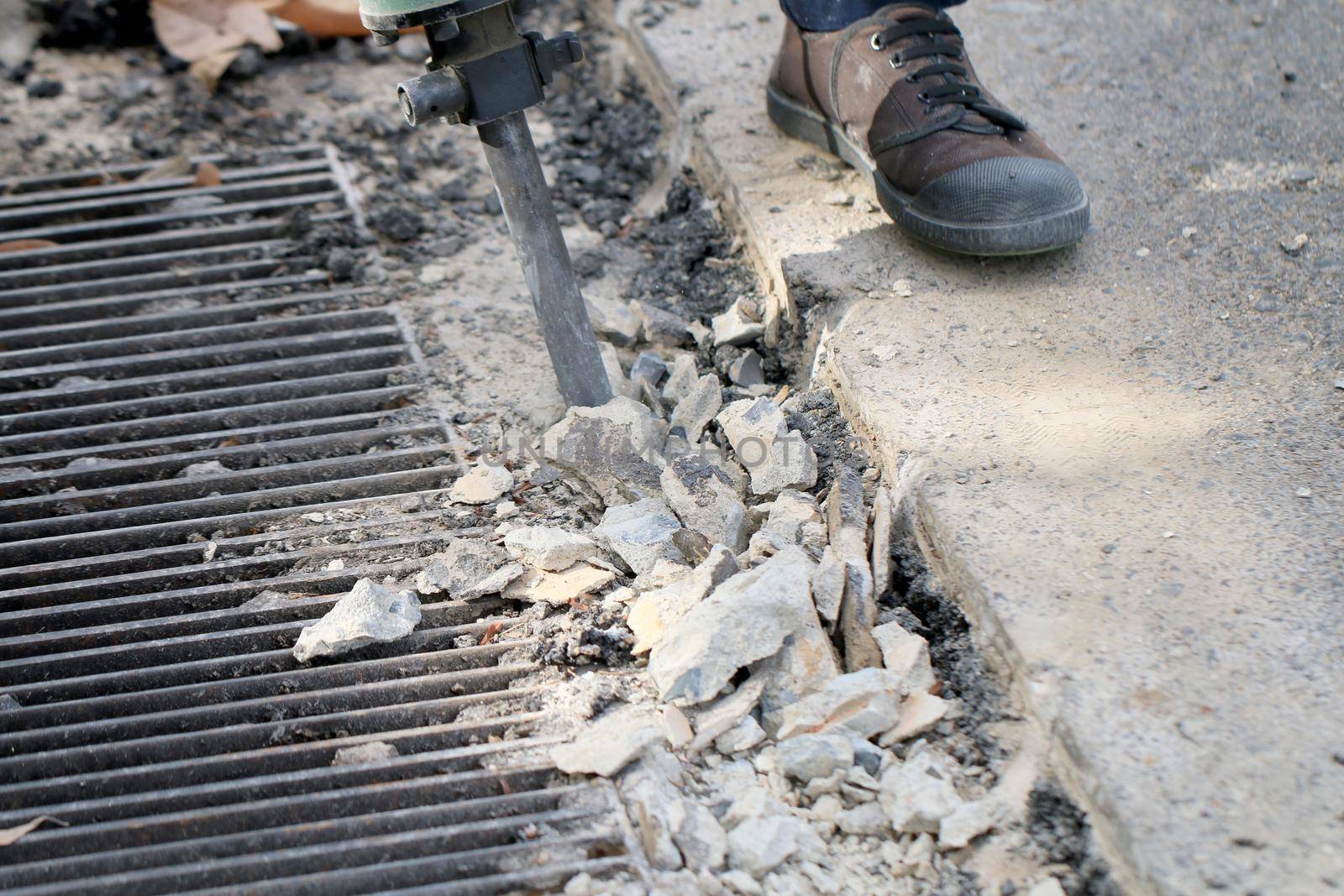 Male workers use electric concrete breaker for digging and drilling concrete repairing driveway surface with jackhammer at the local city road, during sidewalk, work construction site.