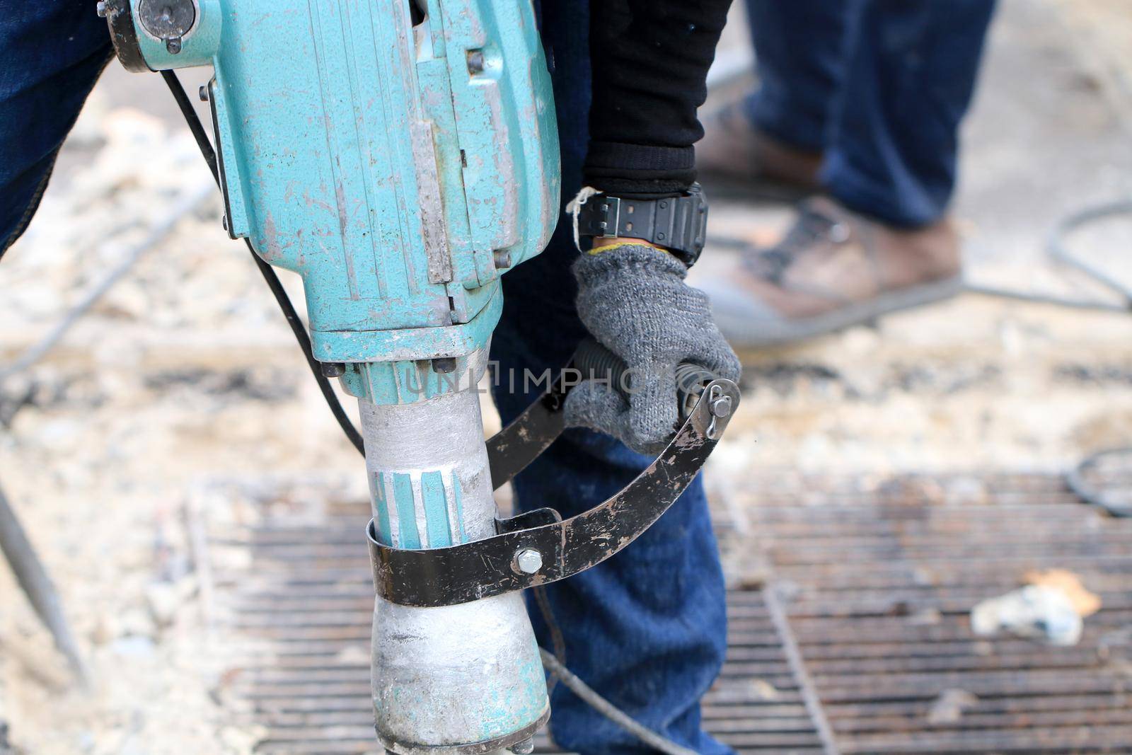 Male workers use electric concrete breaker for digging and drilling concrete repairing driveway surface with jackhammer at the local city road, during sidewalk, work construction site.