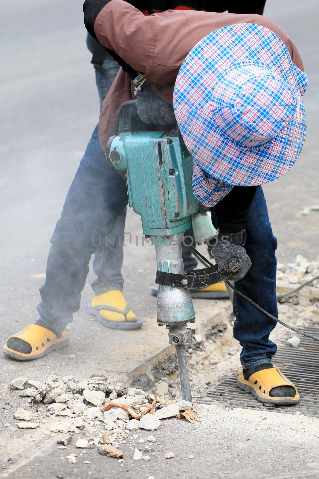 Male workers use electric concrete breaker for digging and drilling concrete repairing driveway surface with jackhammer at the local city road, during sidewalk, work construction site.