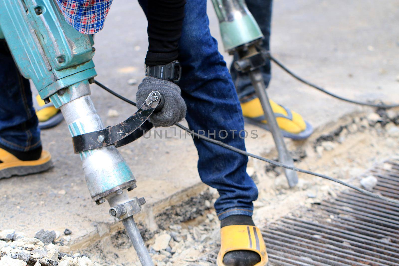 Male workers use electric concrete breaker for digging and drilling concrete repairing driveway surface with jackhammer at the local city road, during sidewalk, work construction site.