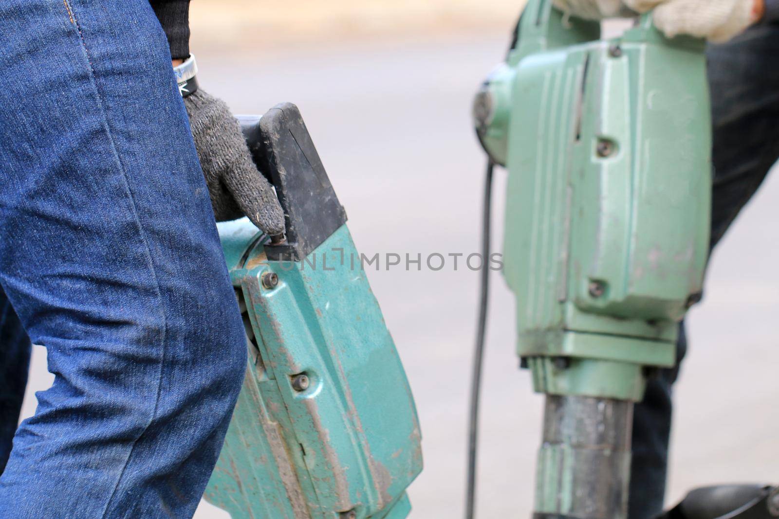 Male workers use electric concrete breaker for digging and drilling concrete repairing driveway surface with jackhammer at the local city road, during sidewalk, work construction site. by NarinNonthamand