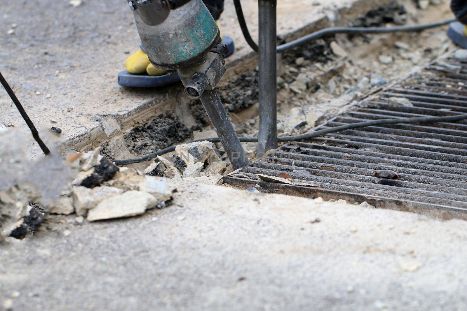 Male workers use electric concrete breaker for digging and drilling concrete repairing driveway surface with jackhammer at the local city road, during sidewalk, work construction site. by NarinNonthamand