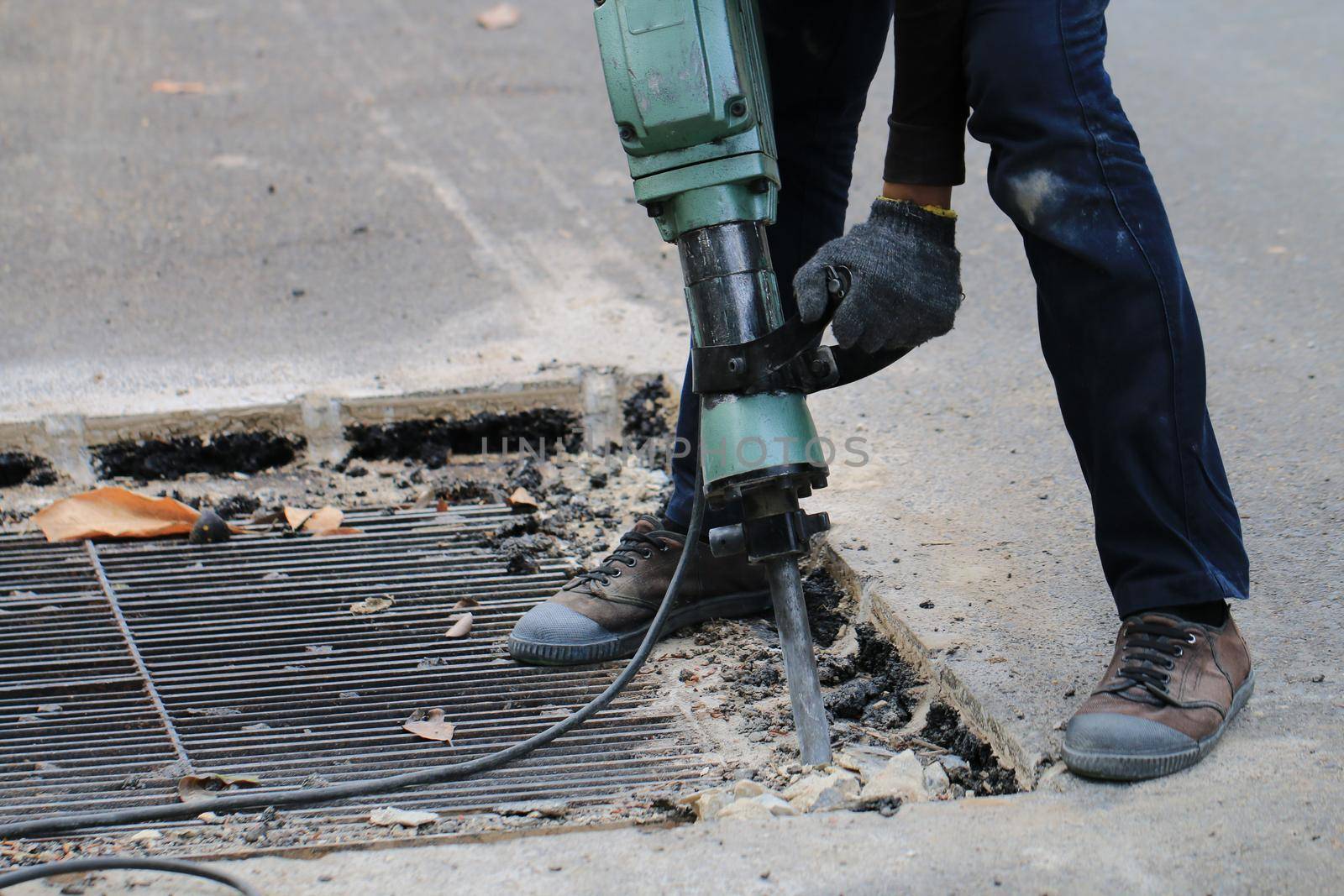 Male workers use electric concrete breaker for digging and drilling concrete repairing driveway surface with jackhammer at the local city road, during sidewalk, work construction site. by NarinNonthamand