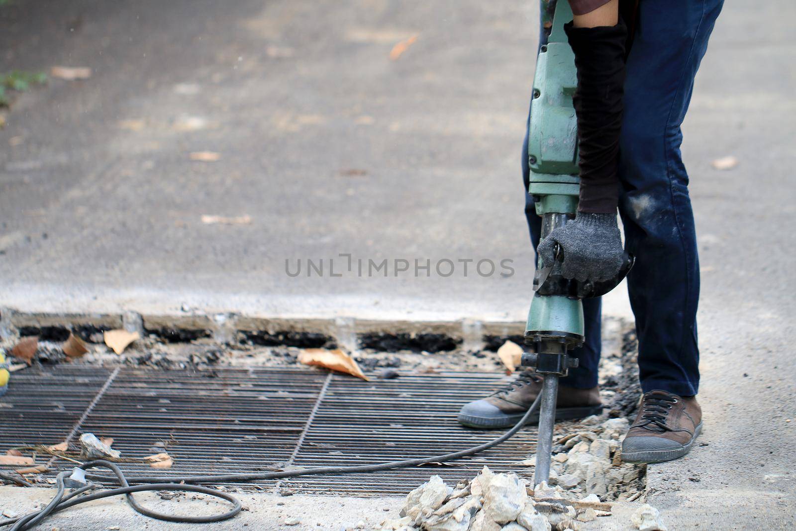 Male workers use electric concrete breaker for digging and drilling concrete repairing driveway surface with jackhammer at the local city road, during sidewalk, work construction site.