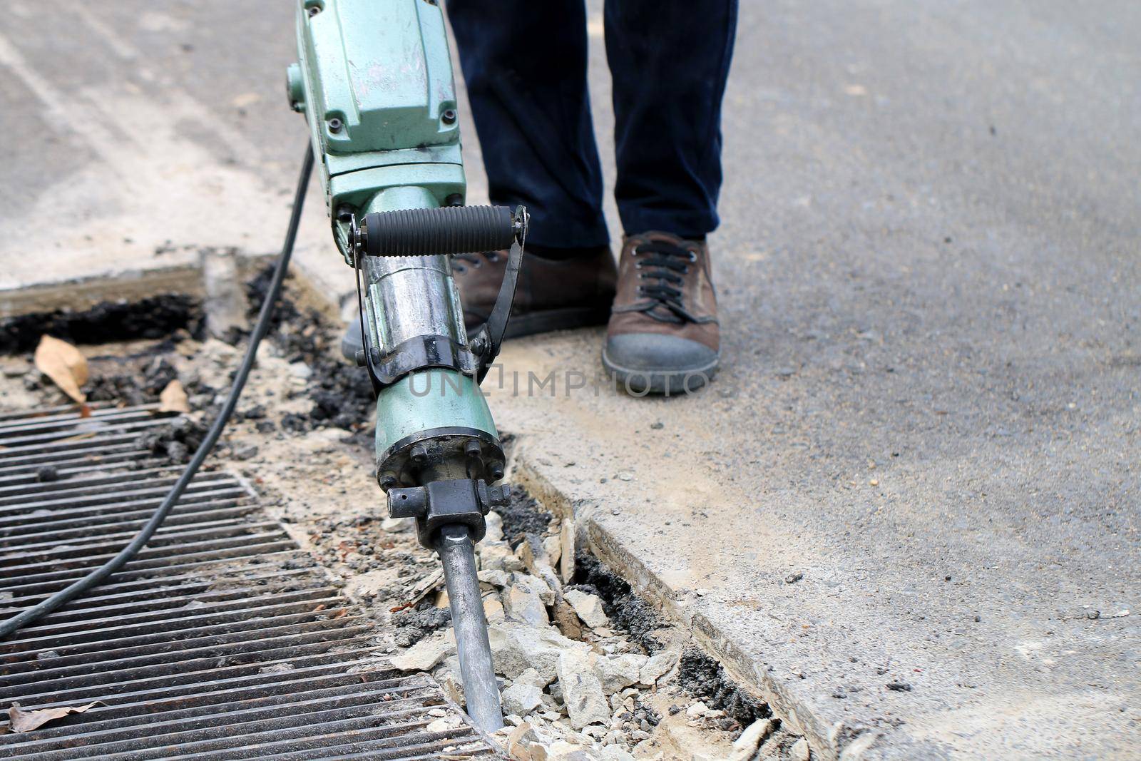 Male workers use electric concrete breaker for digging and drilling concrete repairing driveway surface with jackhammer at the local city road, during sidewalk, work construction site. by NarinNonthamand