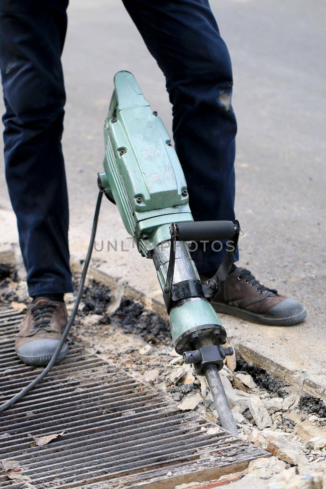 Male workers use electric concrete breaker for digging and drilling concrete repairing driveway surface with jackhammer at the local city road, during sidewalk, work construction site. by NarinNonthamand