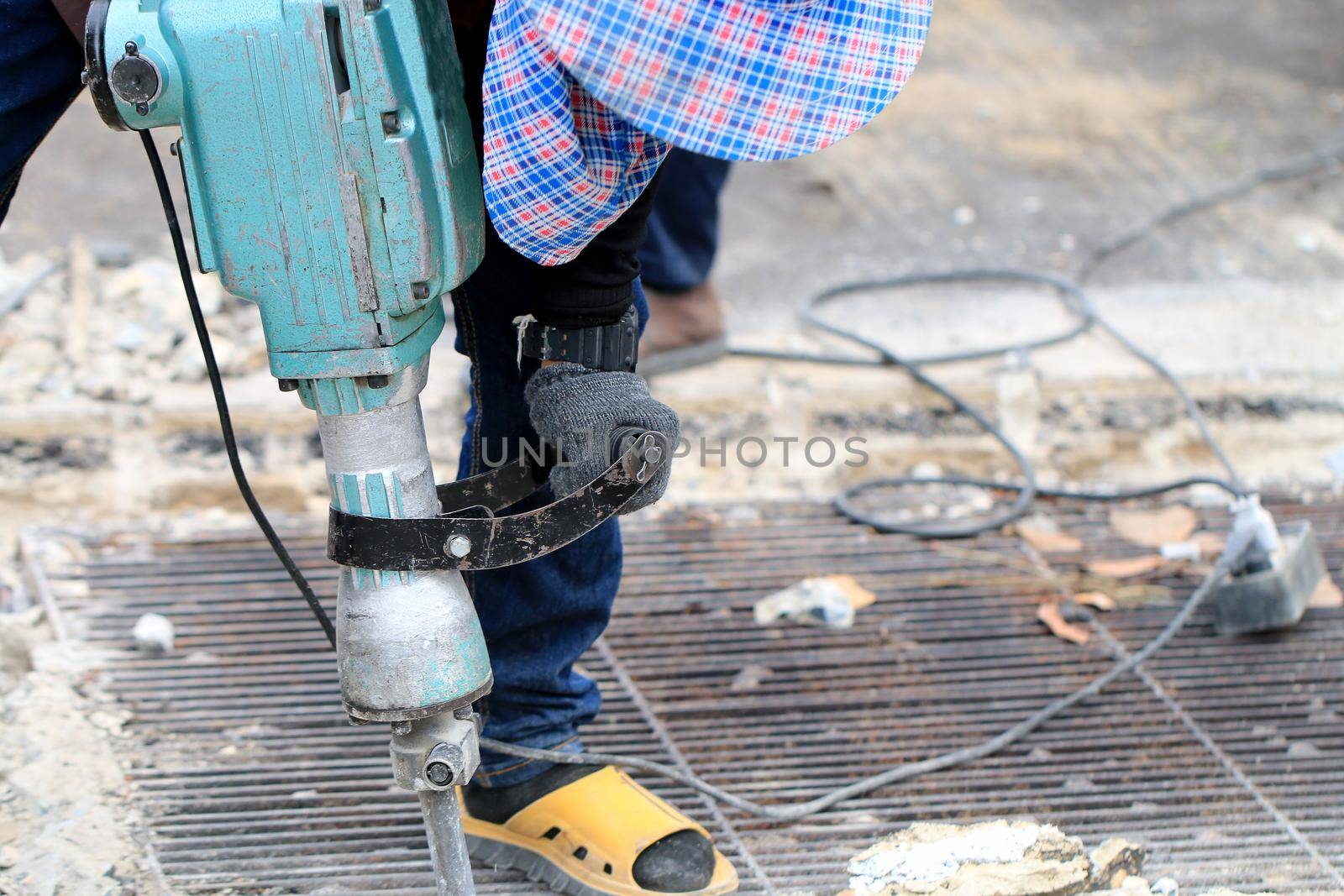 Male workers use electric concrete breaker for digging and drilling concrete repairing driveway surface with jackhammer at the local city road, during sidewalk, work construction site. by NarinNonthamand