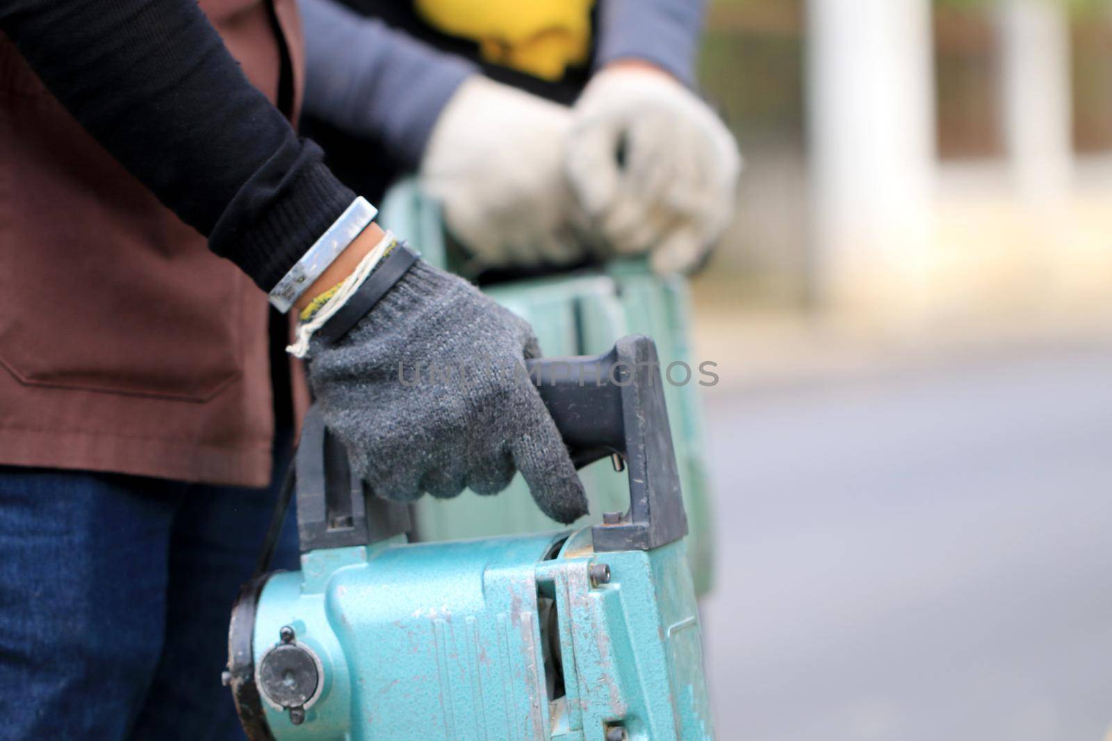 Male workers use electric concrete breaker for digging and drilling concrete repairing driveway surface with jackhammer at the local city road, during sidewalk, work construction site. by NarinNonthamand