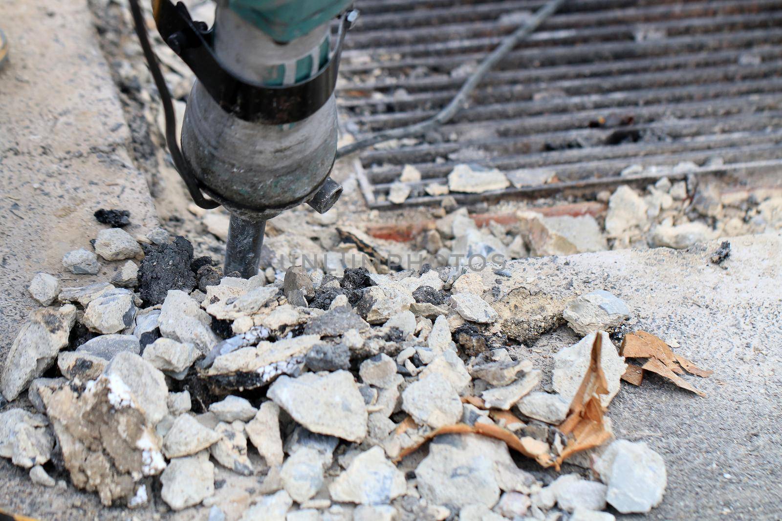 Male workers use electric concrete breaker for digging and drilling concrete repairing driveway surface with jackhammer at the local city road, during sidewalk, work construction site. by NarinNonthamand