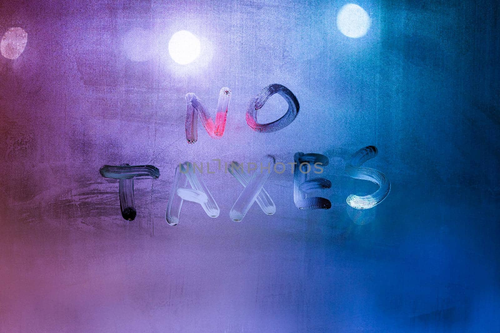 words no taxes handwritten on night wet window glass surface with blue and purple colors in blurry background