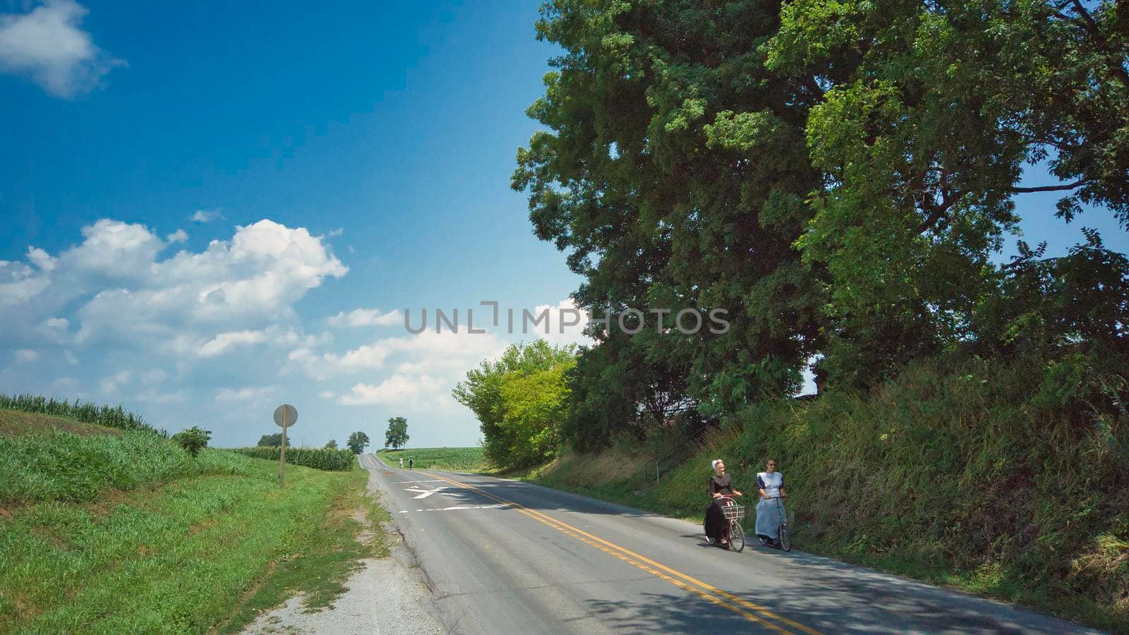 Ronks, Pennsylvania, July 2020 - 2 Amish Women Riding Scooters on a Road on a Summer Day