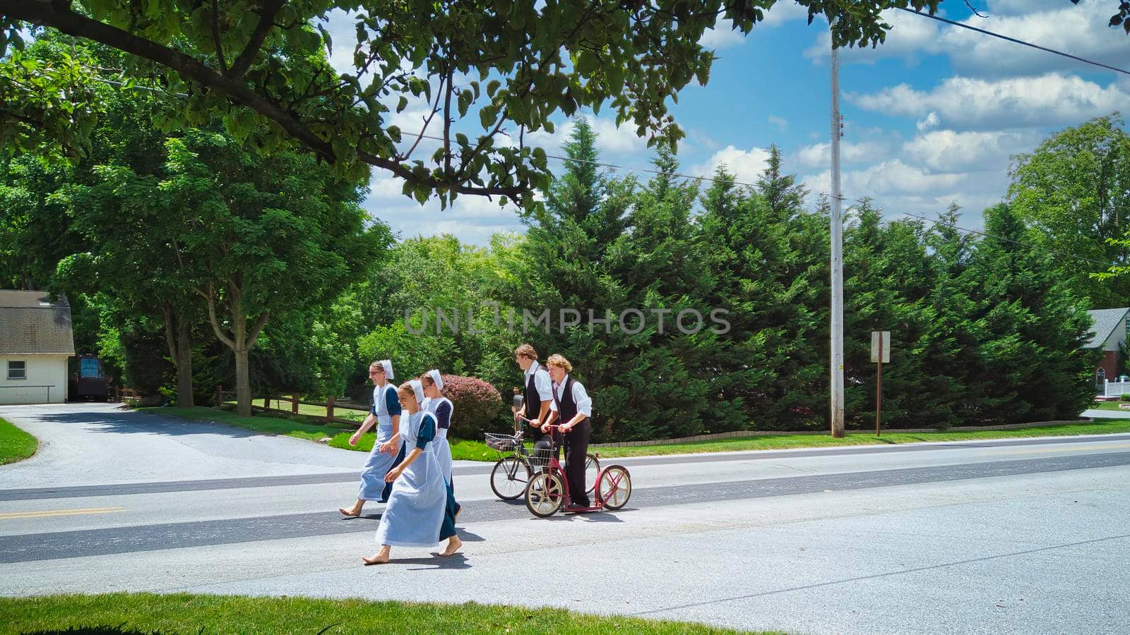 Gordonville, Pennsylvania, June 2020 - A Group of Amish Teenagers Walking and Riding Scooters along a Country Road