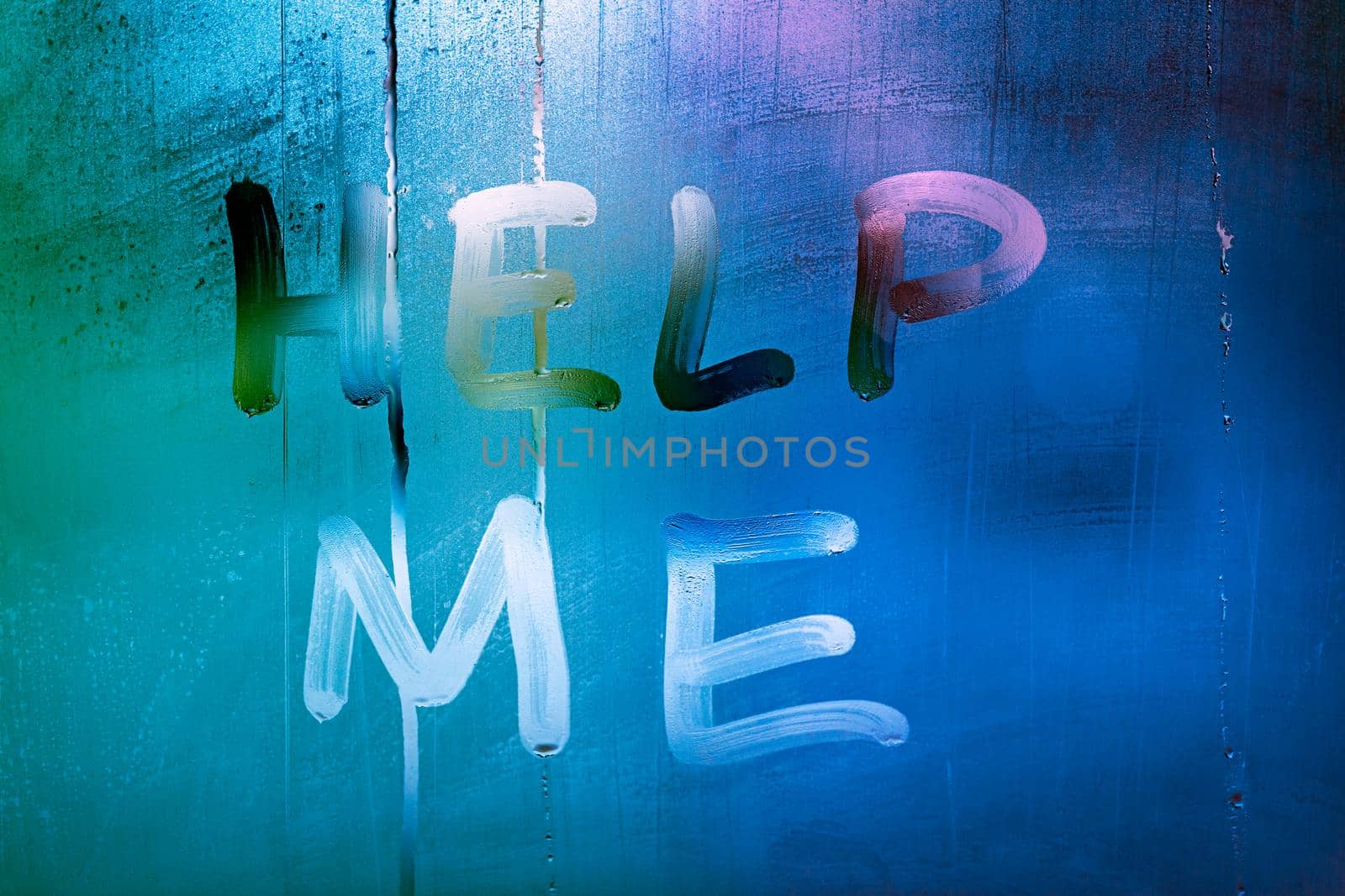the words help me handwritten on night wet window glass with green and blue color gradient in blurry background