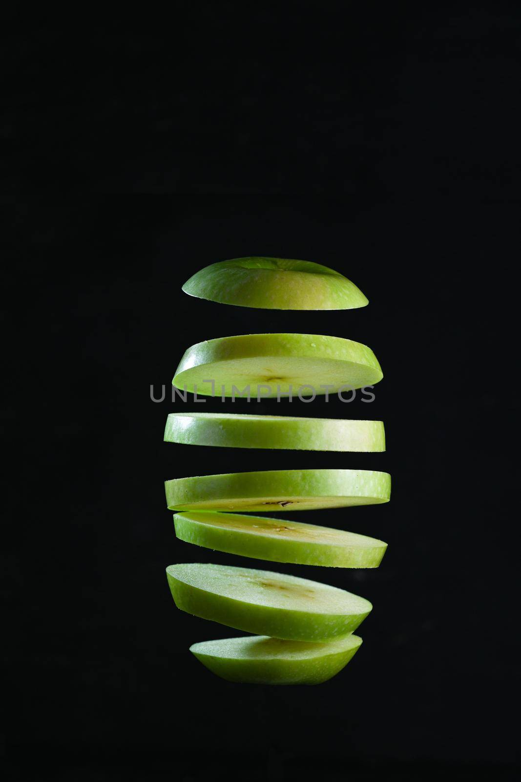 Sliced green apple levitates on black background.