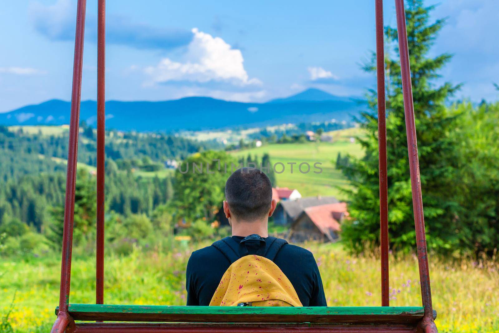 The guy tourist sit on the swing and enjoy amzing nature landscape of summer Karpaty mountains.