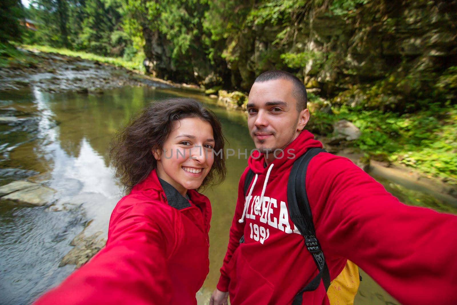 Couple in red shirts posing against background river in the summer mountain forest by Try_my_best