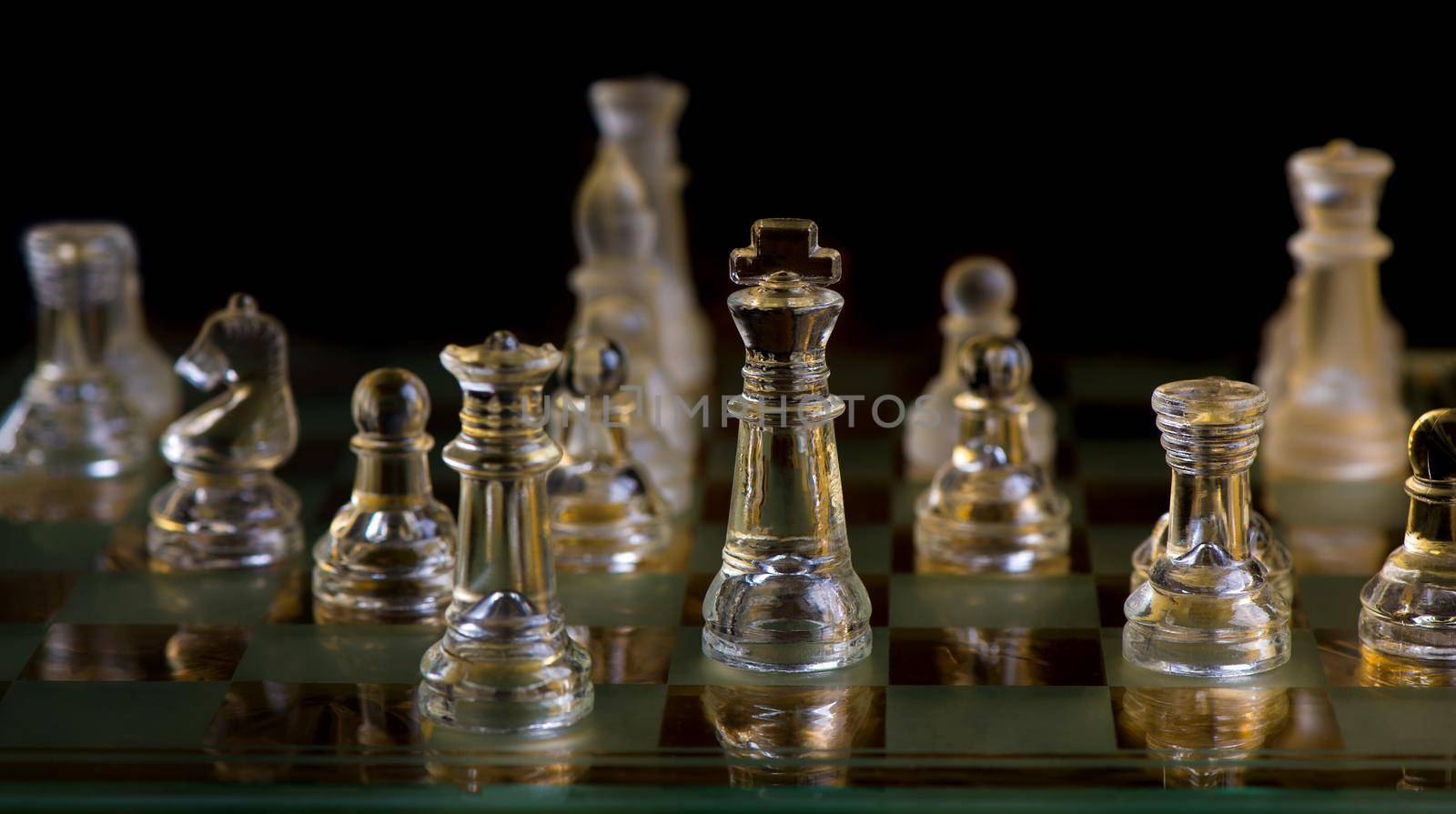 glass chess pieces are defending the king on board in dark by aprilphoto