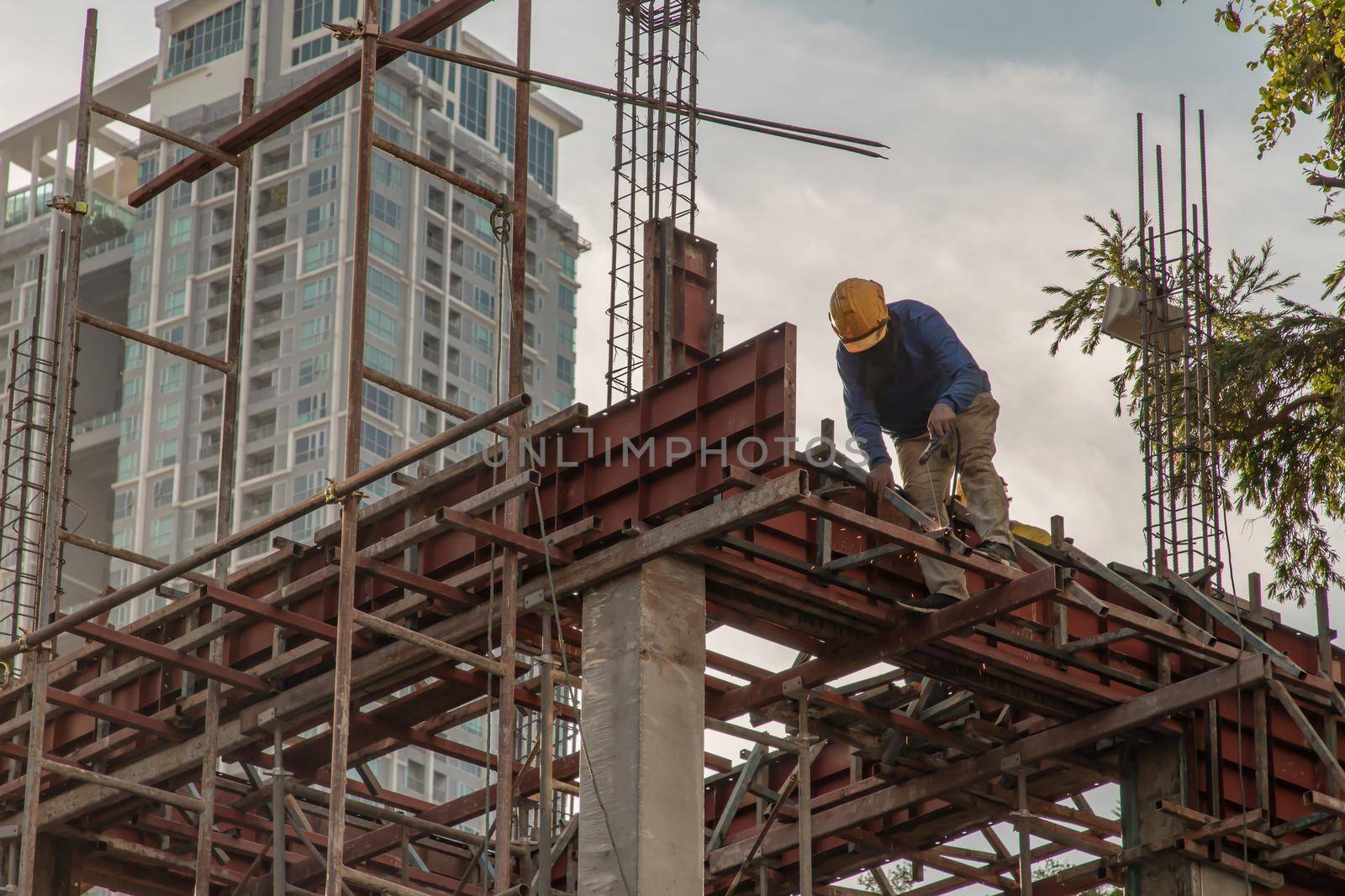 Construction Worker Welding soldering metal girders and Sparks in a Structure high above at the Construction site. Selective focus.