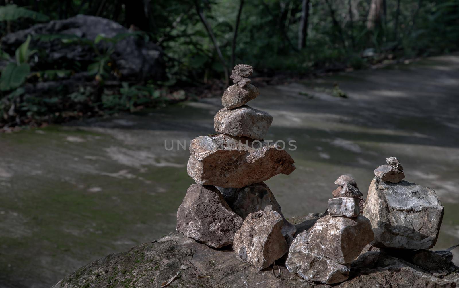 Balanced stone tower on walkway up the mountain with green plants in the background. No focus, specifically.